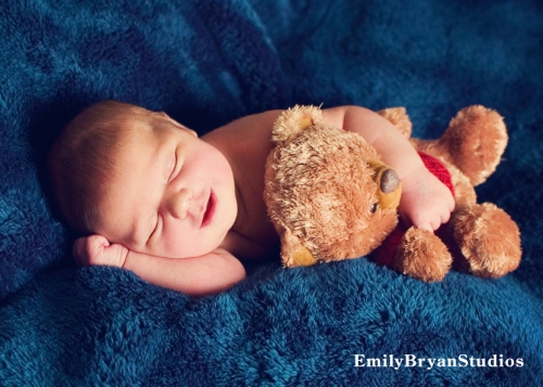 Adorable smiling newborn baby holding a teddy bear.