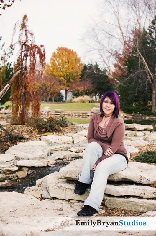 Portrait of Kirsten sitting on rocks in a park.