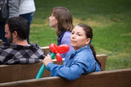 Woman sitting on a bench holding a balloon in the shape of a flower.